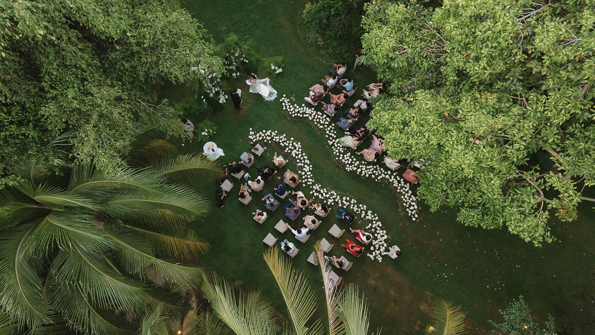 Aerial view of a garden wedding ceremony with a white flower-lined aisle among tropical trees near Ho Chi Minh City